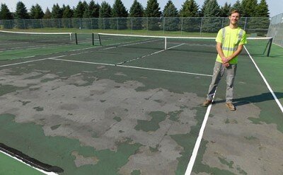 Jake Chopp, a maintenance II employee for the city of Stewartvilles public works department, stands at one of four time-worn Bear Cave Park tennis courts scheduled to be resurfaced next spring.
