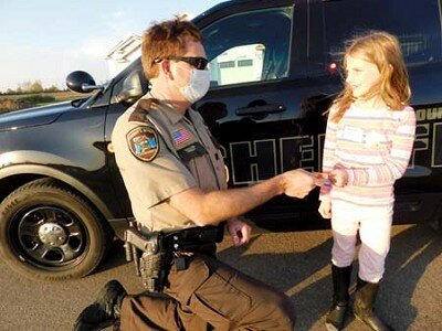 Nora Picker, 8, a second grader at the Central Education Center, accepts a sticker from Jason Owen, Stewartville’s community oriented policing (COPS) deputy, at a National Night Out party on Tuesday evening, Oct. 6.