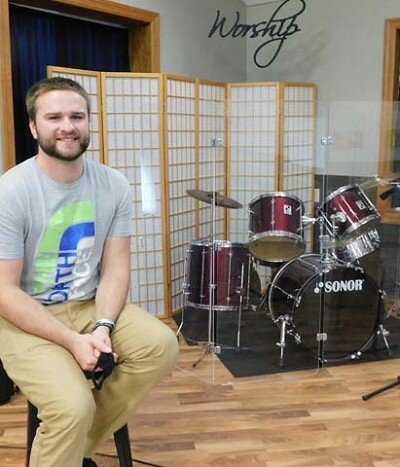 Aaron Regnier , the new associate pastor of student ministries at Grace Evangelical Free Church, poses near the drum set used at Grace Church’s Sunday services.