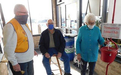 Gussie Redfield of Rochester drops a donation into the Salvation Army’s red kettle as Stewartville Lions Club bell ringer Dave Nystuen, left, and non-Lion volunteer Dick Koenigs look on.
