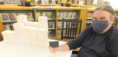 Nate Deprey, director of the Stewartville Public Library, holds a version of a PDF flash drive, which contains the same information as the 65 rolls of microfilm stacked at left. Residents can now use the flash drive to search for historical information from the Stewartville STAR.
